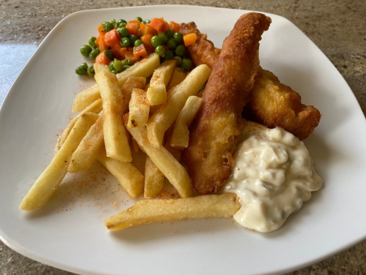 A plate of fish and chips served with peas, carrots, and tartar sauce.