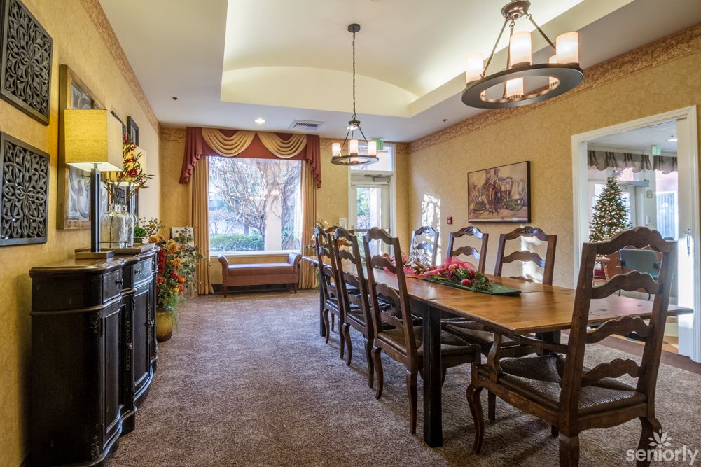 A cozy dining room with a long wooden table and elegant chairs, illuminated by chandeliers.