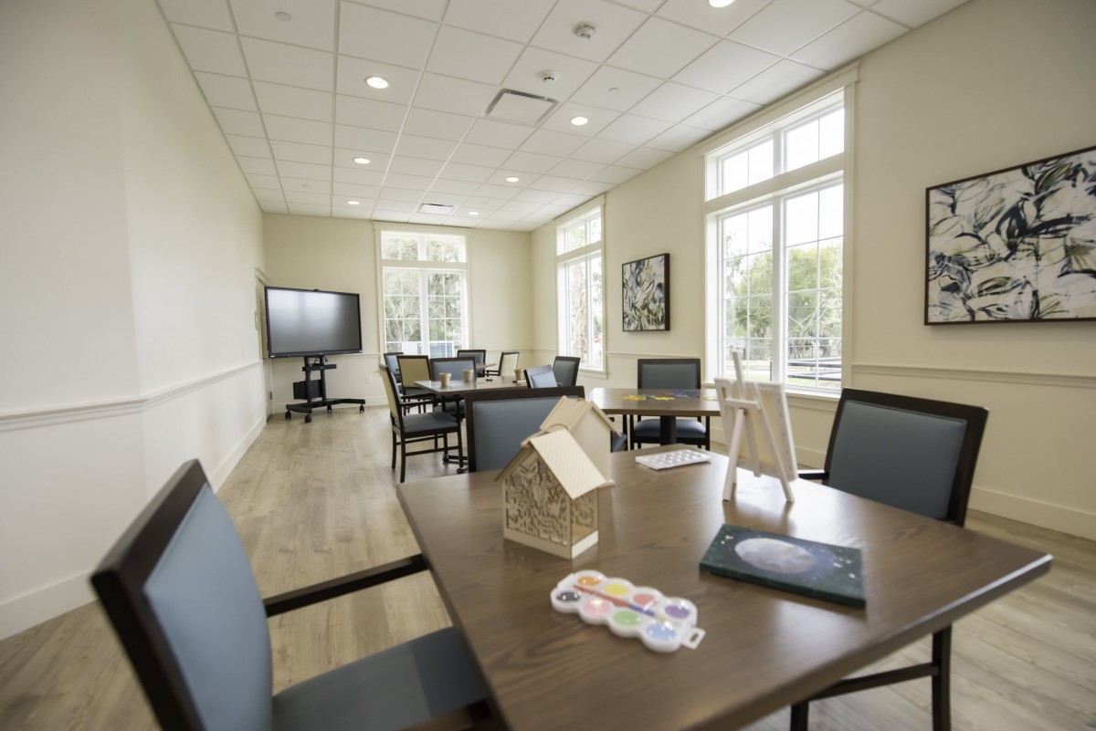 A bright and modern meeting room with tables, chairs, and a TV.