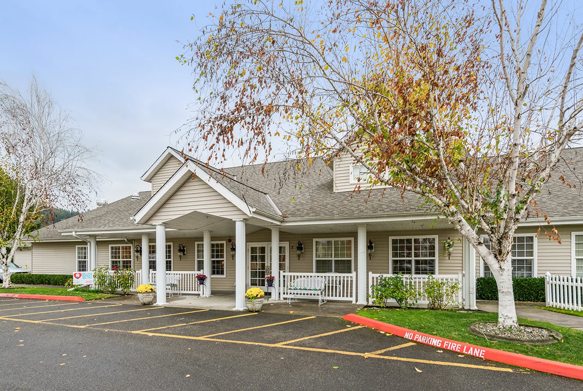 A residential building with a covered entrance, surrounded by trees and a parking area.