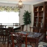 A dining room with a large table, ornate chairs, and a wooden bookshelf.