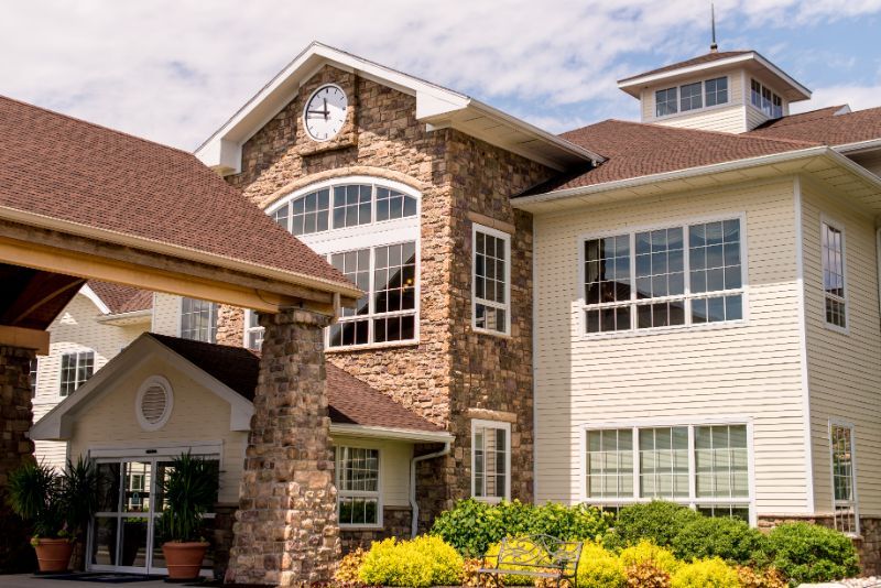 A residential building with a stone facade and large windows, featuring a clock above the entrance.