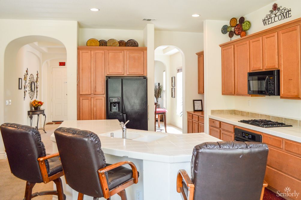 A modern kitchen interior with wooden cabinets, a black refrigerator, and bar stools around the island.