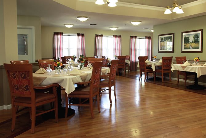 A well-arranged dining room with tables and chairs, featuring a wooden floor and natural lighting.