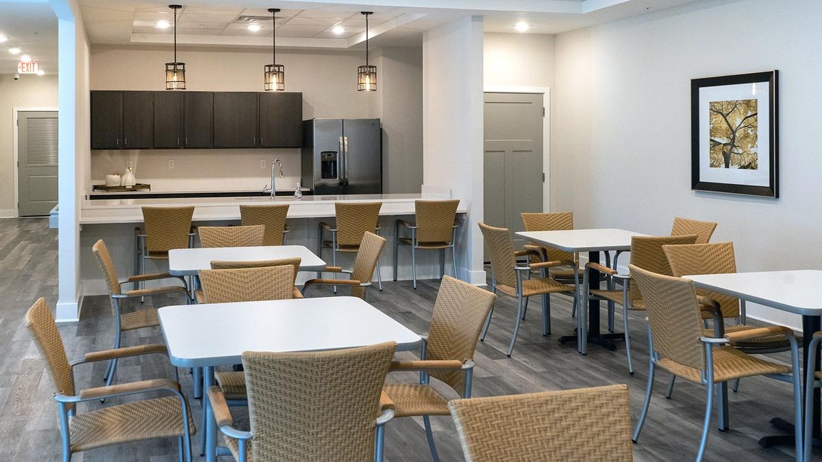 A modern cafeteria with tables and chairs, adjacent to a kitchen area.