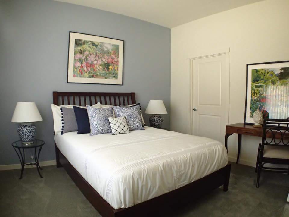 A neatly arranged bedroom featuring a bed with multiple pillows, framed artwork on the walls, and bedside lamps.