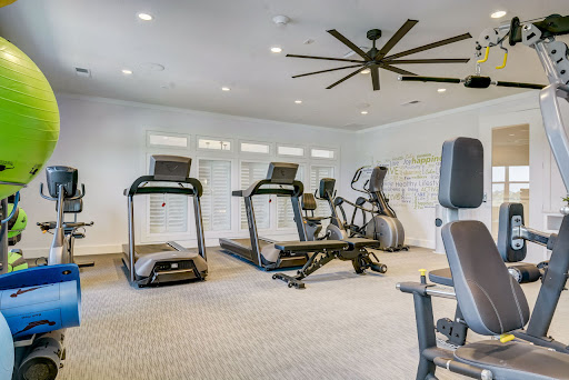 A well-equipped gym featuring treadmills, an elliptical machine, and strength training equipment in a bright, spacious environment.
