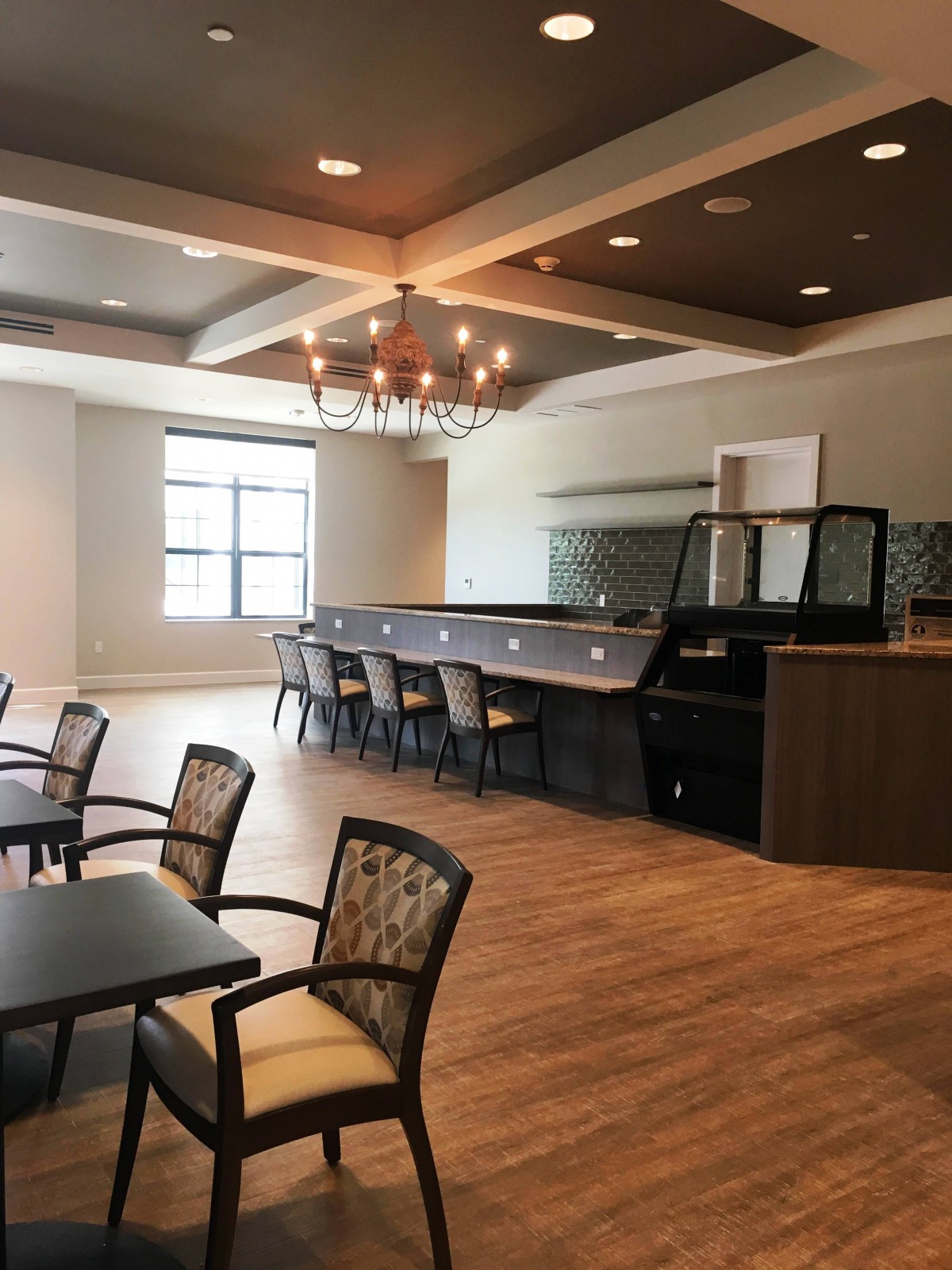 A modern bar and seating area with a chandelier and wood flooring.