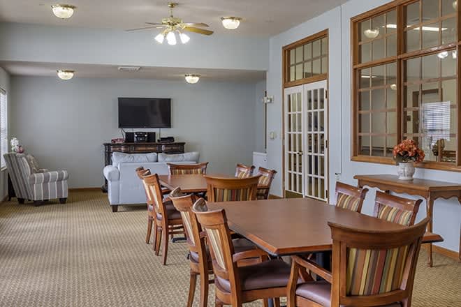 A spacious dining area with wooden tables and chairs, featuring a TV and ceiling fans in a well-lit room.