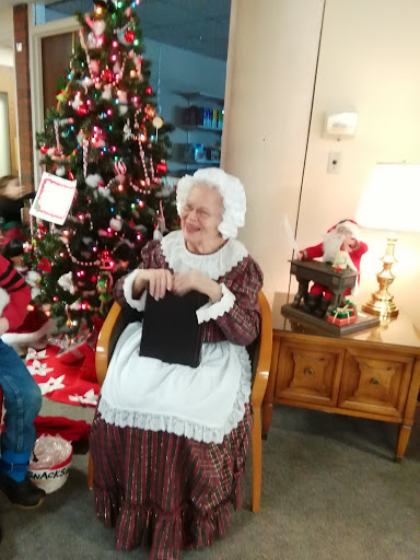 An elderly woman in traditional attire enjoys knitting by the Christmas tree.