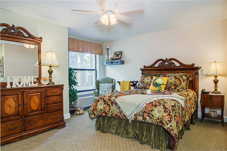 A cozy bedroom with traditional decor, featuring a wooden bed and dresser, floral bedding, and a ceiling fan.