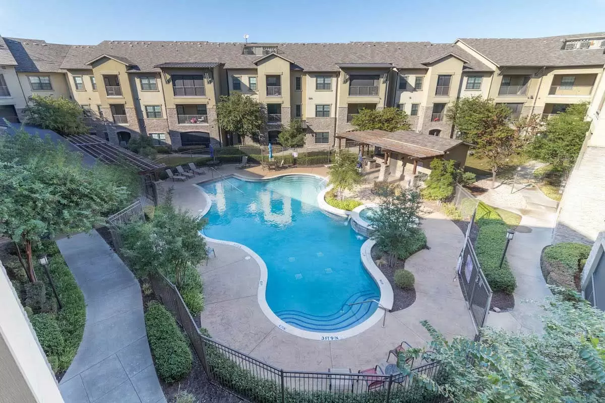 Aerial view of an apartment complex with a central swimming pool surrounded by landscaped pathways.