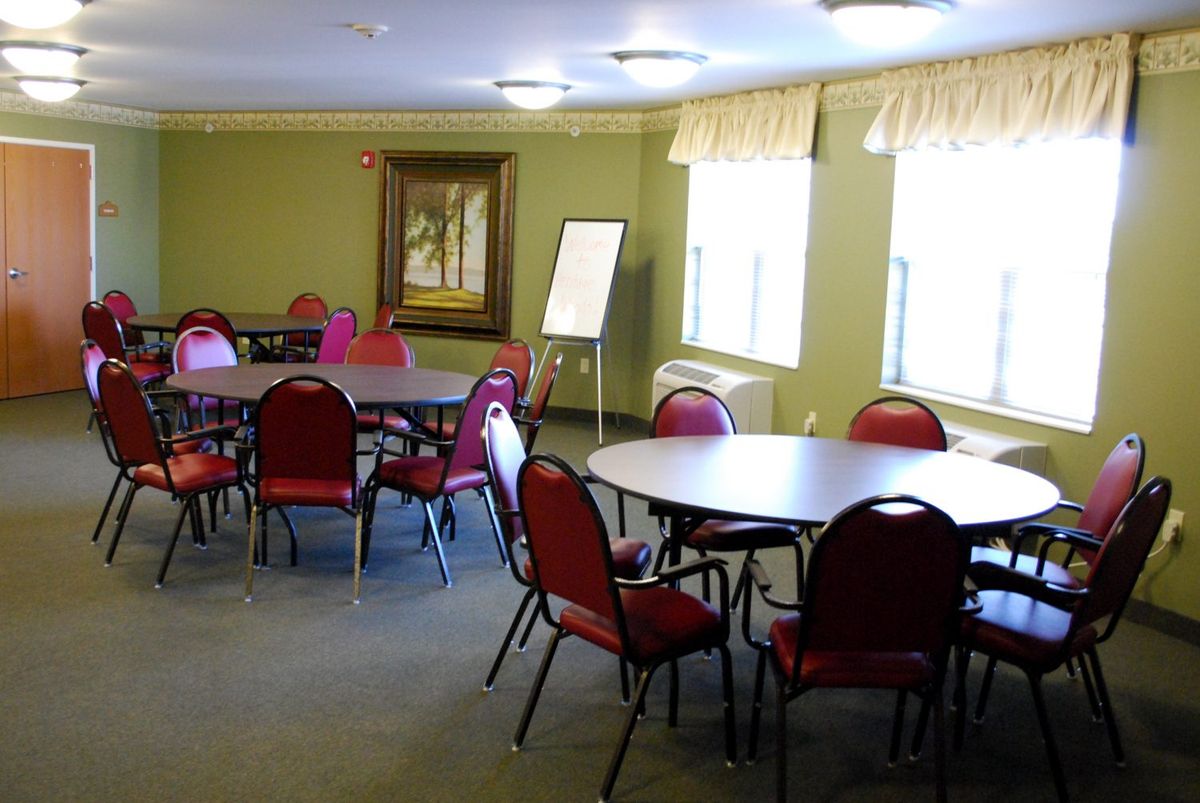 An empty meeting room with round tables and red chairs, featuring large windows and a flip chart.