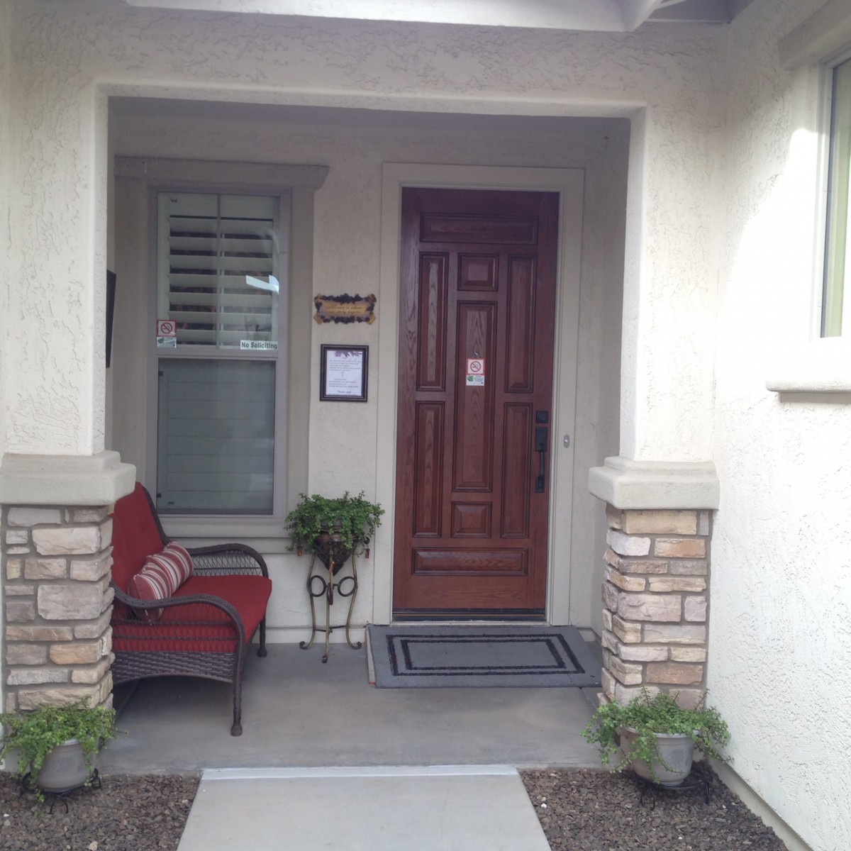 A cozy front porch with a wooden door, a chair, and decorative plants.