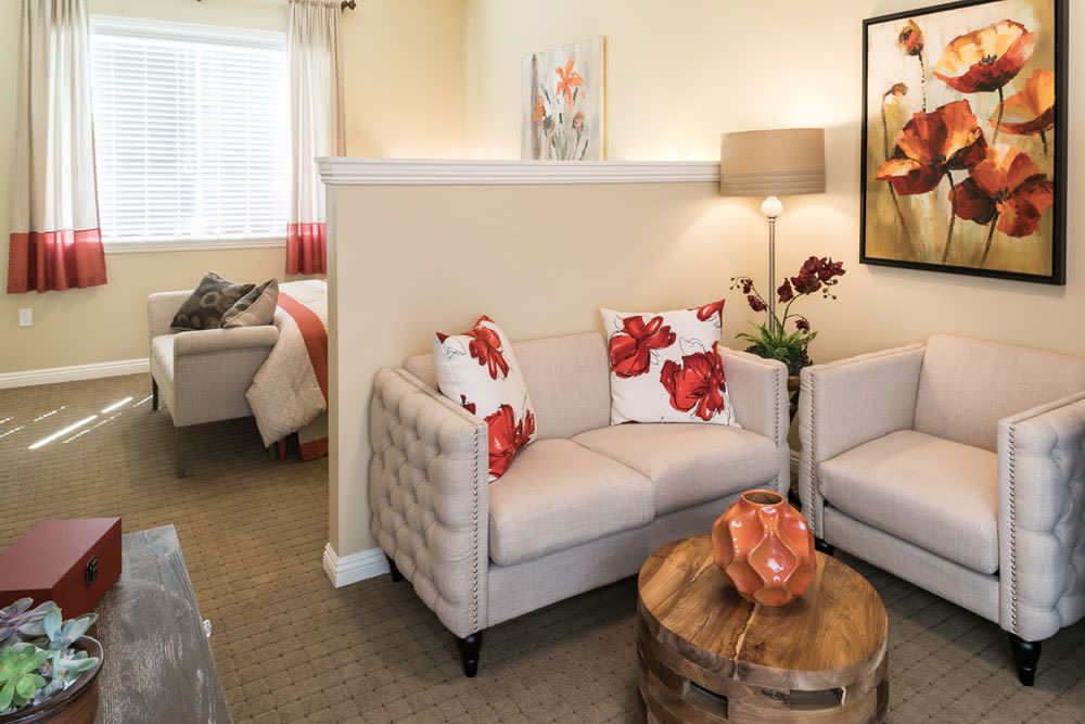 A cozy living room with two tufted sofas, bright floral pillows, a round wooden table, and contemporary artwork.