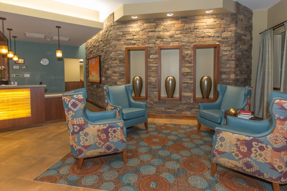 A stylish lobby with blue armchairs, colorful floral-patterned seating, decorative vases, and a stone accent wall.