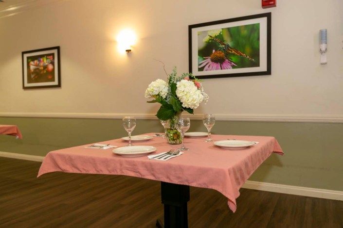 An elegantly set dining table with a pink tablecloth, adorned with a floral centerpiece and surrounded by art on the walls.