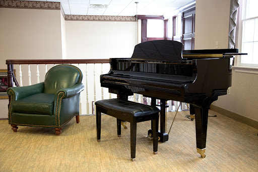 A black grand piano accompanied by a green armchair in a cozy interior setting.