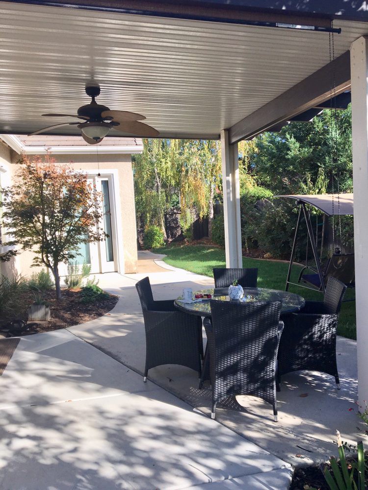 A cozy outdoor patio with a dining set under a covered area, surrounded by greenery.