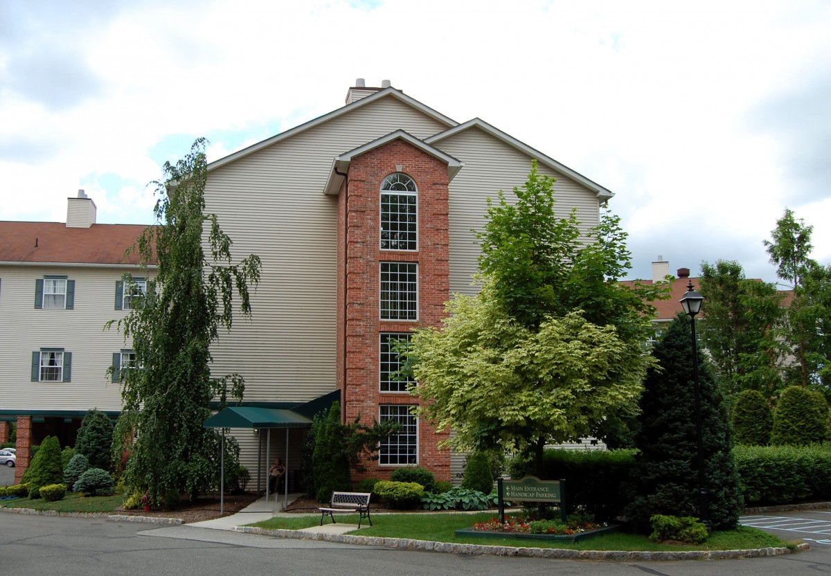 A residential apartment building surrounded by green trees and a small garden.