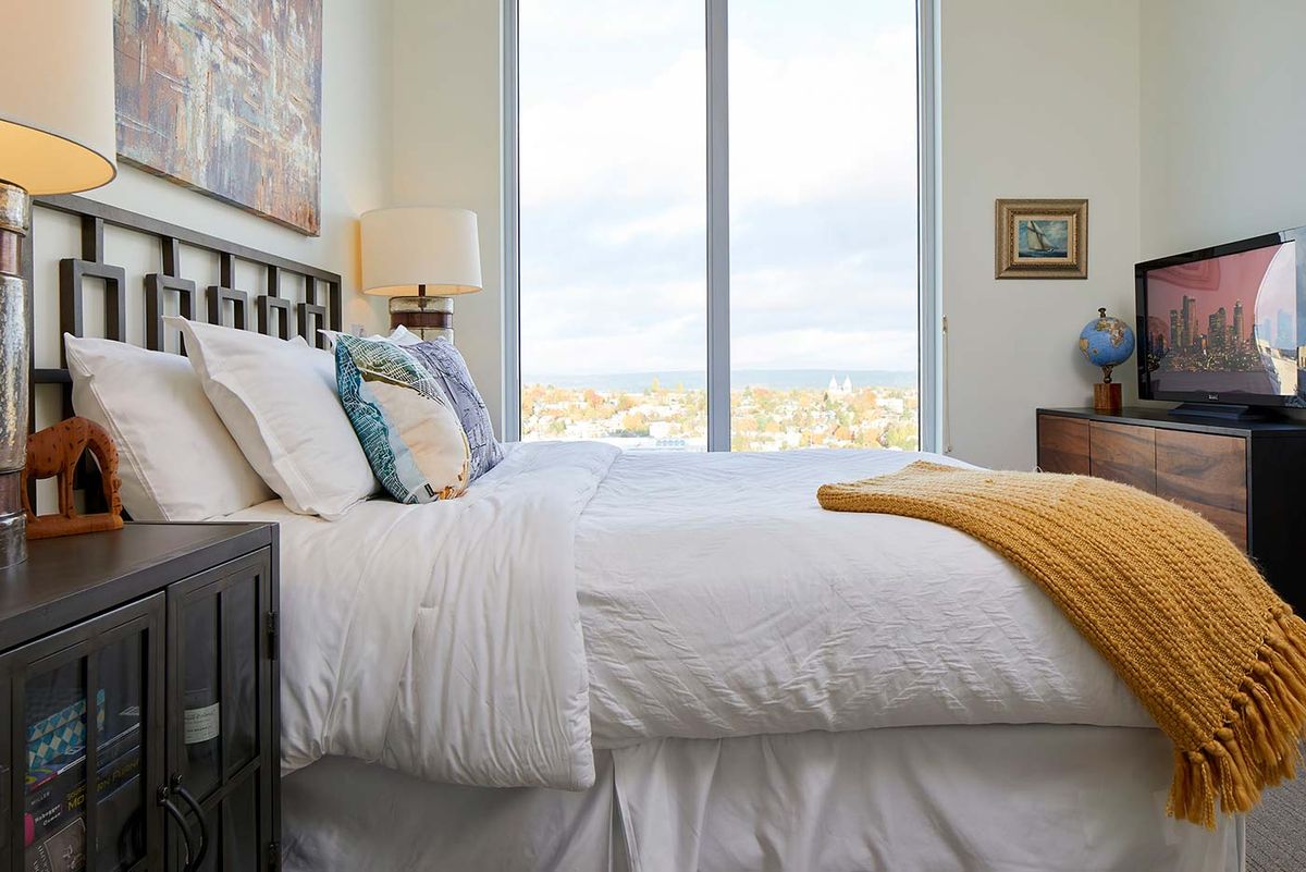 A modern bedroom with a neatly made bed and a large window offering a scenic view.