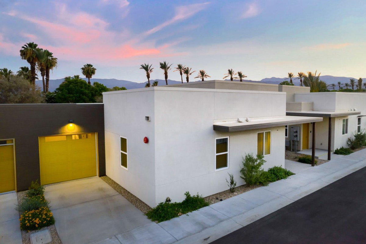 Modern minimalist house exterior at sunset with palm trees in the background.