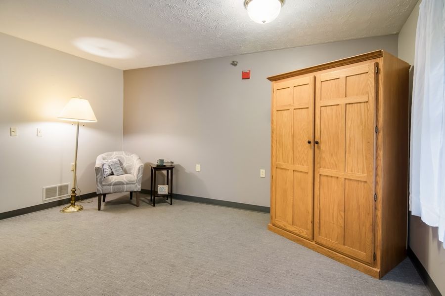 A simple room interior with a wooden wardrobe, an armchair, and a floor lamp.