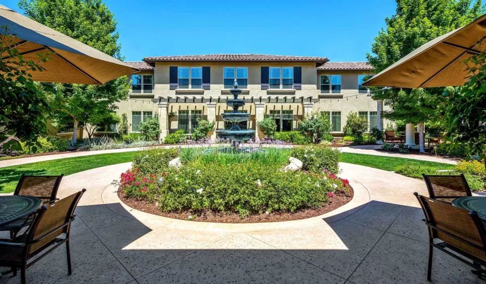 A landscaped garden with a central fountain in front of a large building.