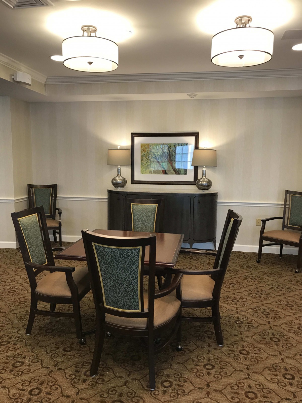 A well-furnished meeting room with a central table surrounded by chairs, decorative lamps, and a framed painting on the wall.