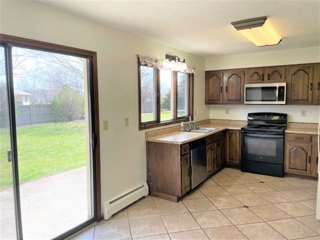 A bright kitchen with wooden cabinets, tile flooring, and modern appliances, featuring a window and a sliding glass door opening to the outside.