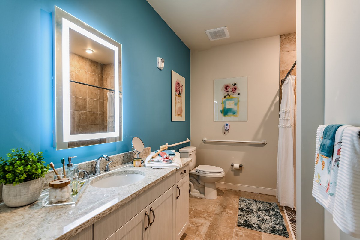 A modern bathroom with a blue accent wall, featuring a large mirror, dual sinks, and a shower area.