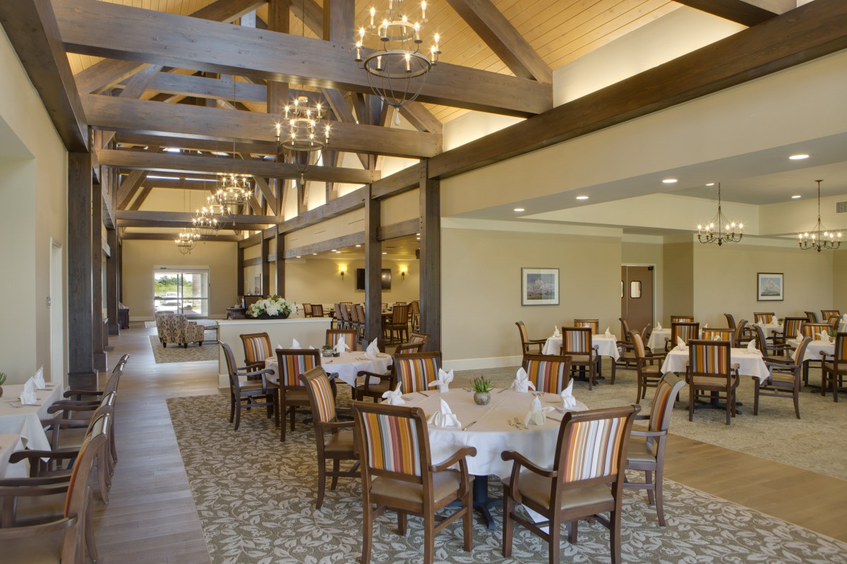A spacious dining area with wooden beams, chandeliers, and neatly arranged tables and chairs.