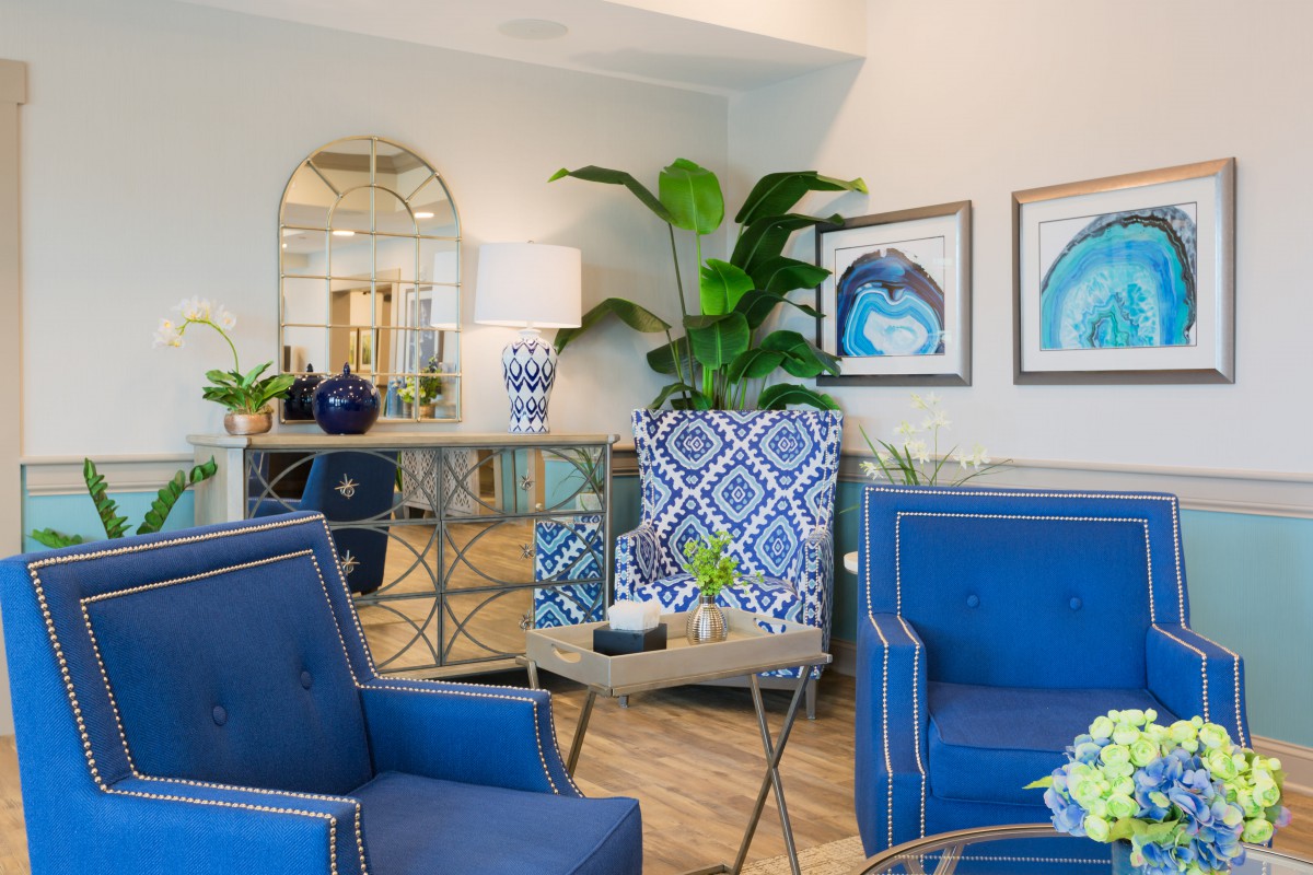 A stylish living room featuring blue armchairs and geometric patterned accents, enhanced by modern artwork and lush greenery.