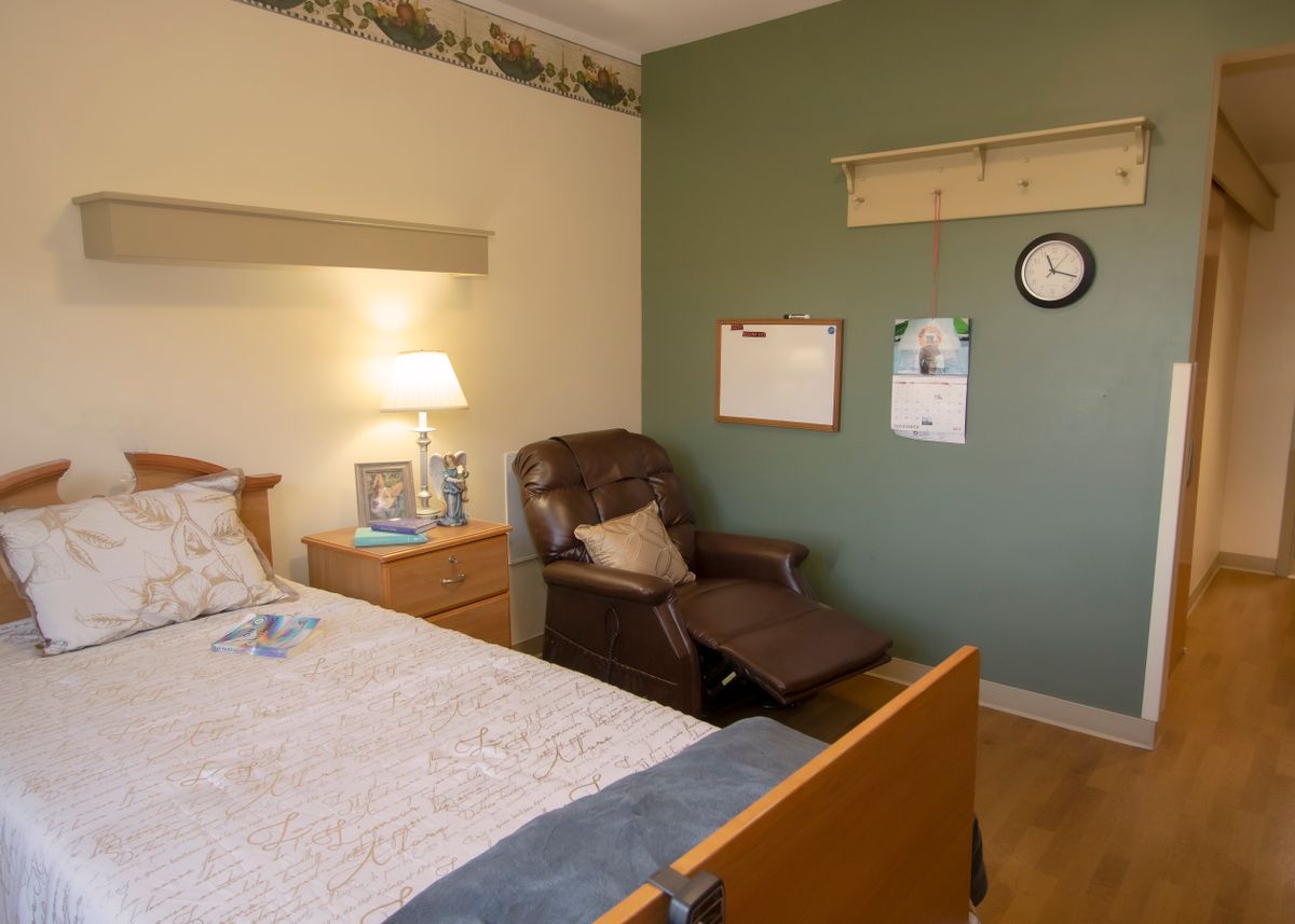 A cozy bedroom interior featuring a bed, lamp, and reclining chair against a green accent wall.