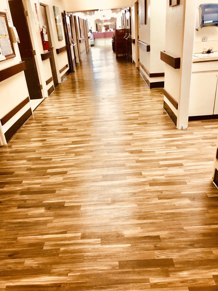 A spacious hospital corridor with wooden flooring.