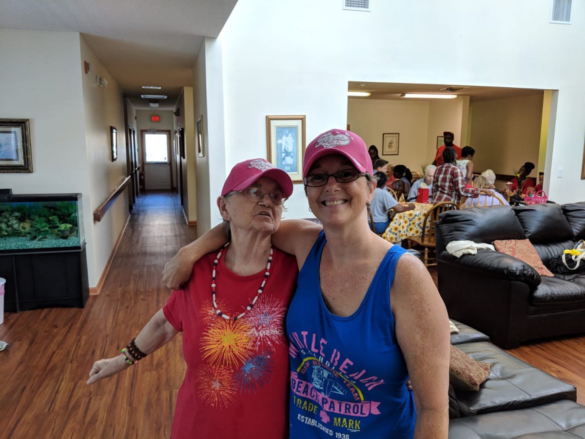 Two friends wearing hats and casual outfits pose happily indoors.