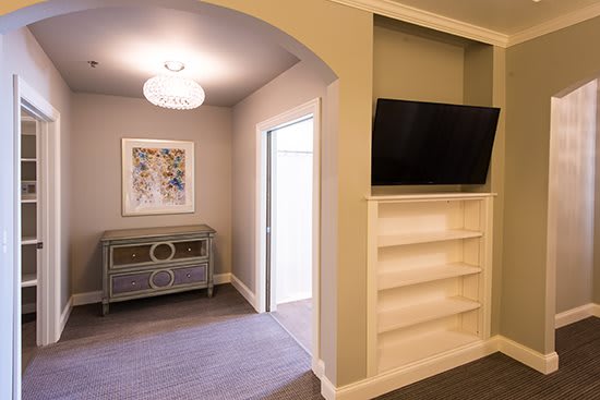 A modern living area with a television mounted above a built-in bookcase, leading to a hallway with decorative furniture.