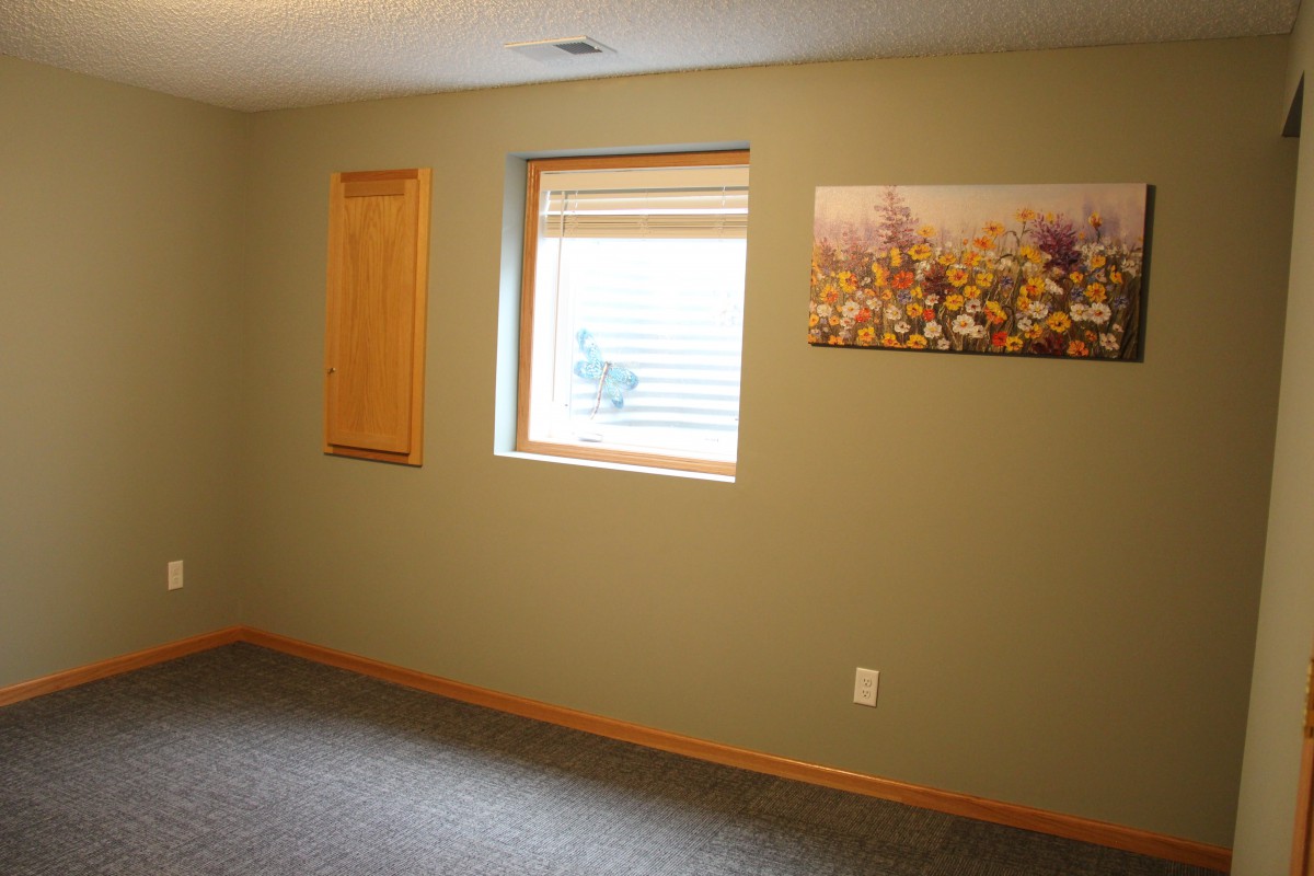 An empty basement room with beige walls, a window, and wall art.