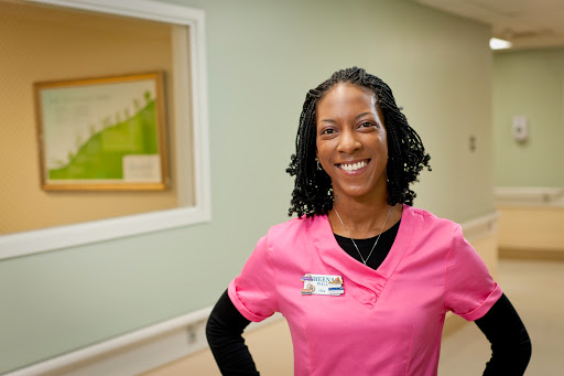 A healthcare professional smiling in a pink uniform, exuding warmth and approachability.