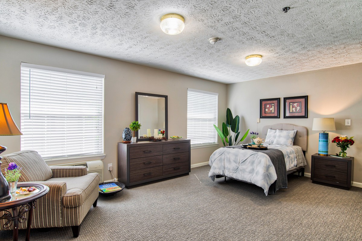 A modern and cozy bedroom featuring a neatly made bed, dresser, armchair, and stylish decor.