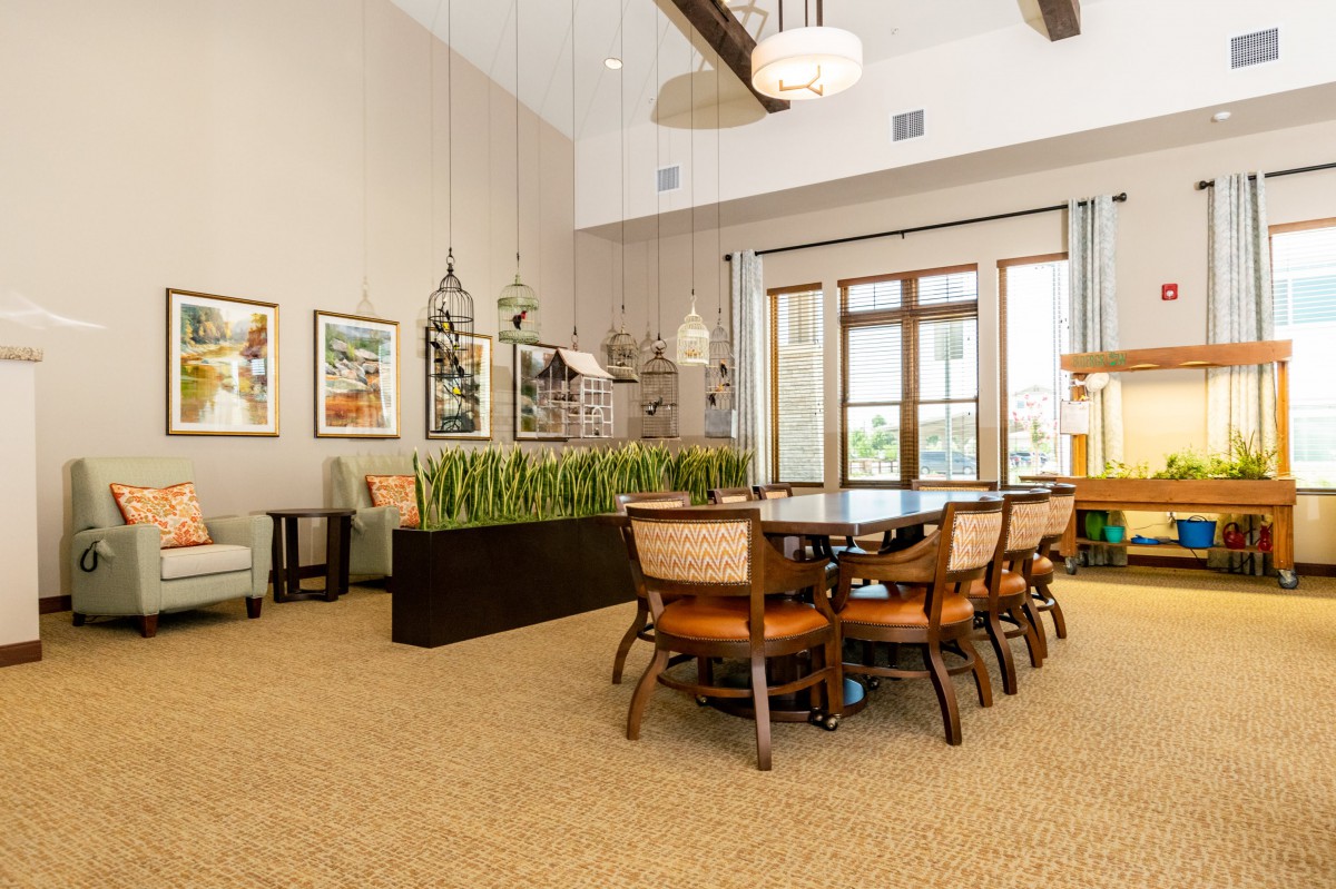 A modern dining room with a large wooden table, surrounded by chairs and decorated with art pieces on the walls and pendant lights hanging from the ceiling.
