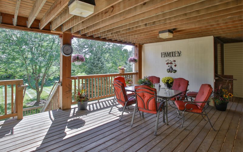 A cozy outdoor patio with a wooden deck and red cushioned chairs overlooking a garden.