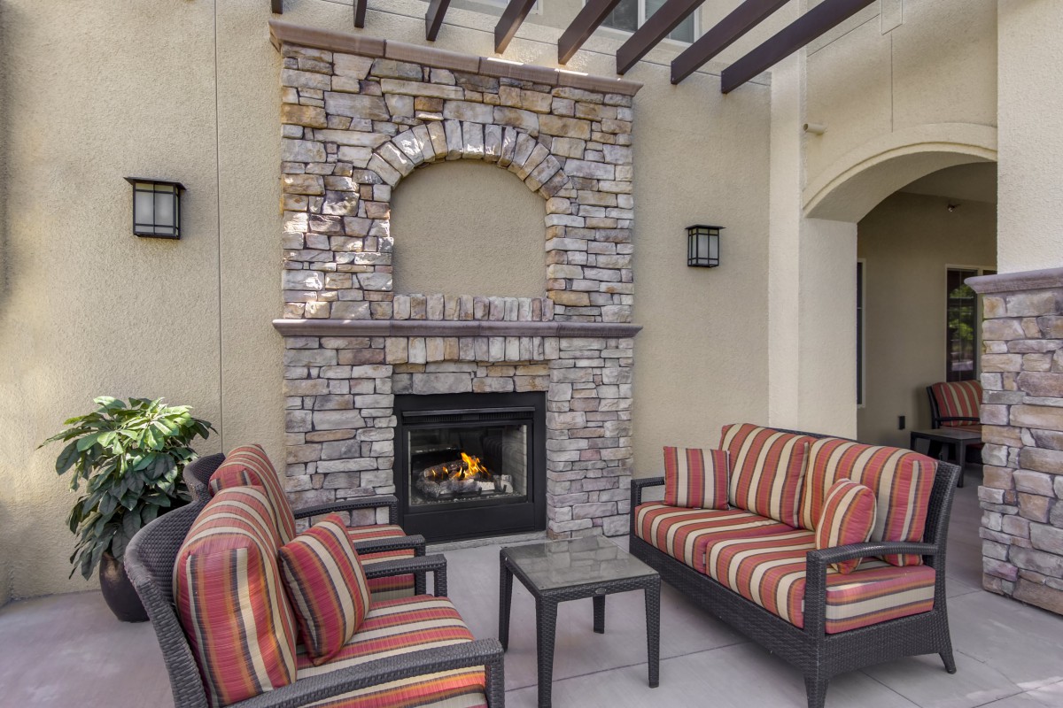 A cozy patio with striped seating and a stone fireplace under a pergola.