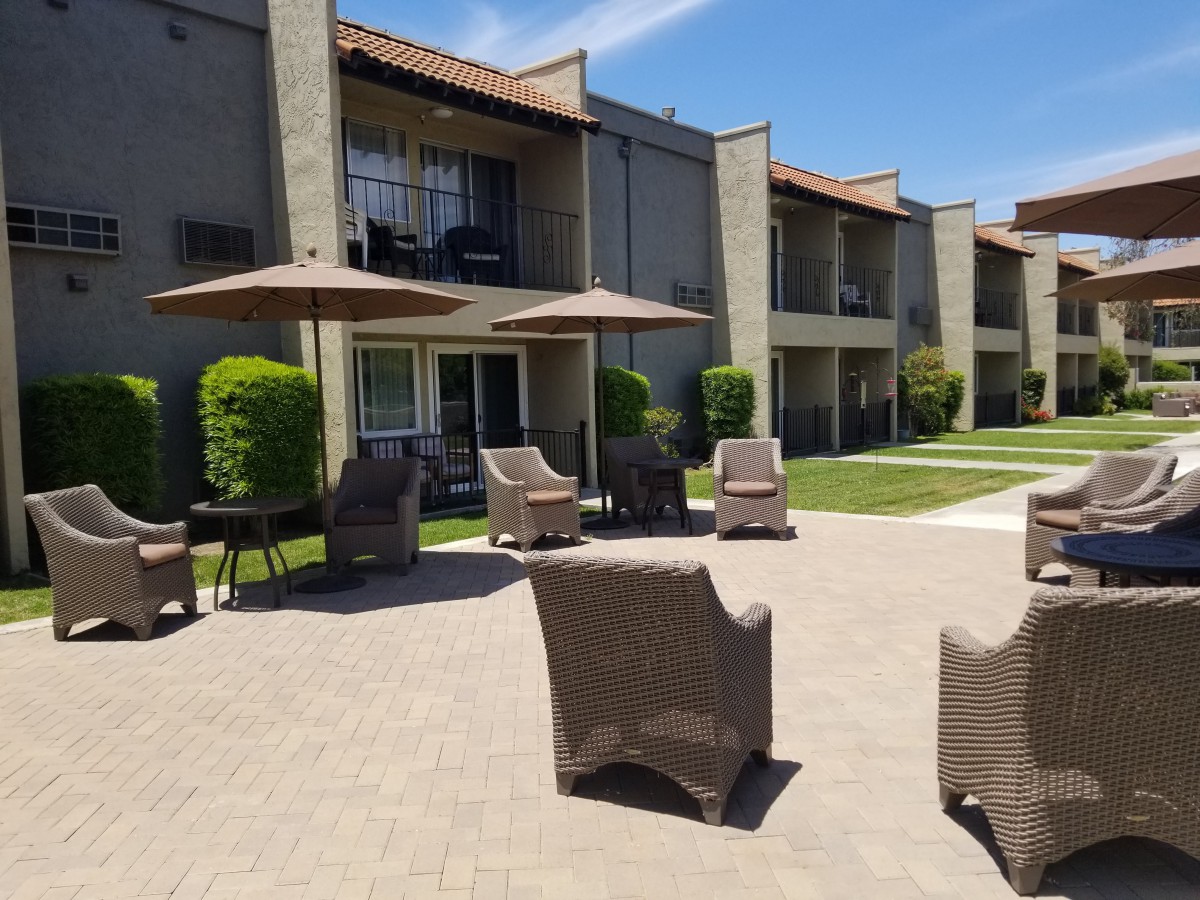 A sunny outdoor patio area with wicker chairs and umbrellas in front of an apartment building.