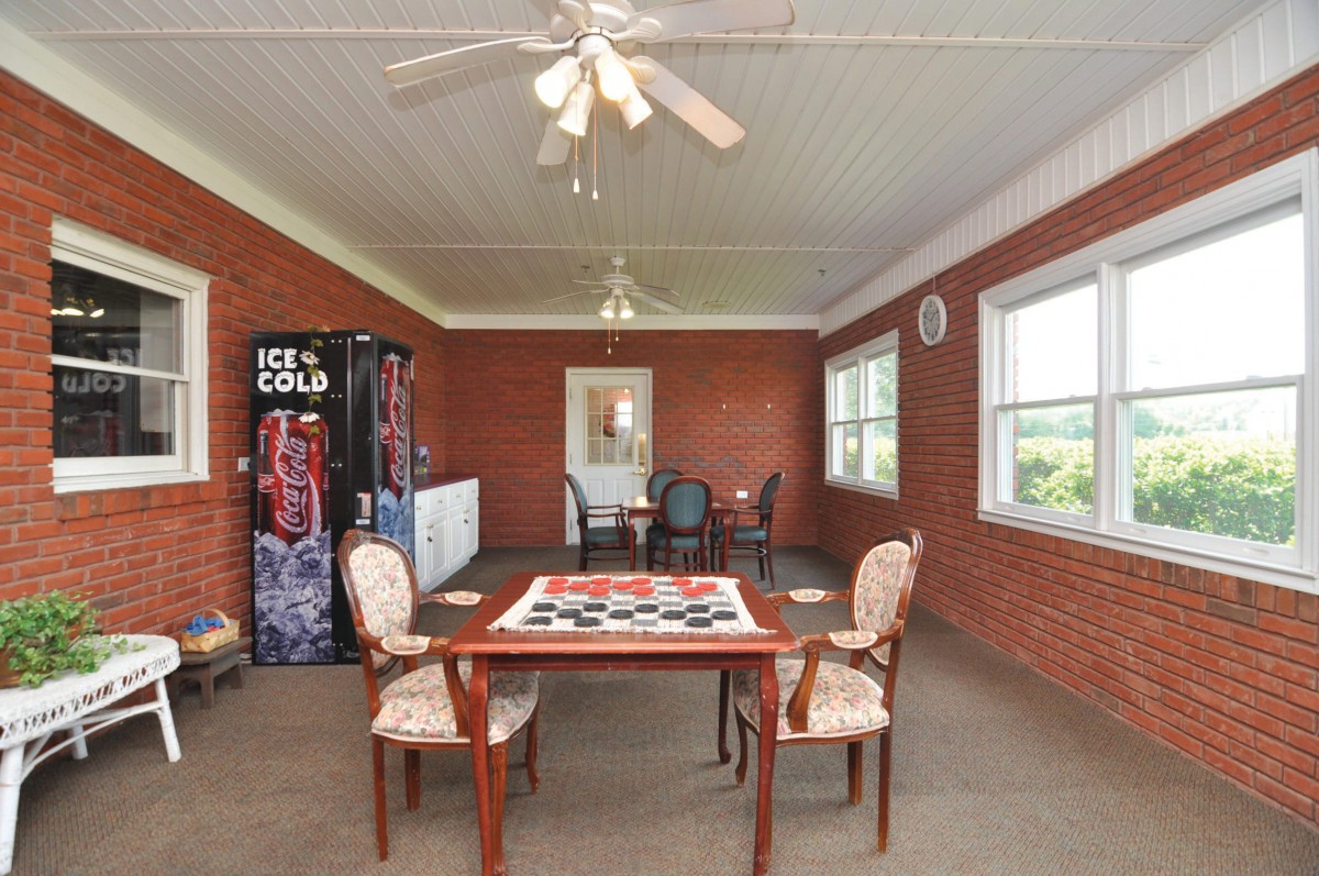 A dining area with a table, chairs, ceiling fan, and vending machine against brick walls.