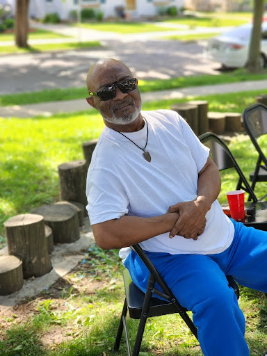A man enjoying a sunny day at the park, dressed casually and relaxing on a chair.