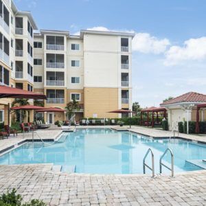A swimming pool in front of a multi-story hotel building under a clear blue sky.
