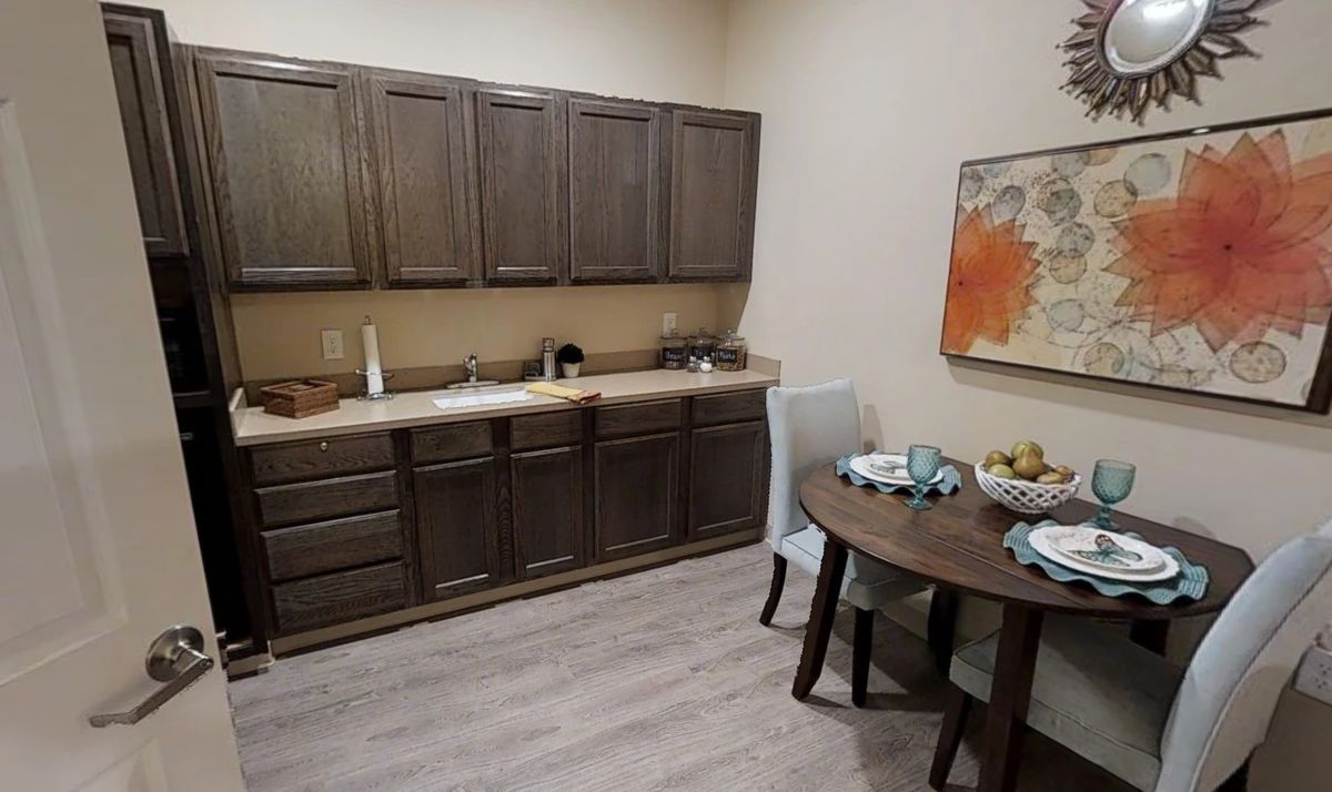 A cozy kitchen area featuring wooden cabinets, a sink, and a small dining table set with chairs and artwork on the wall.