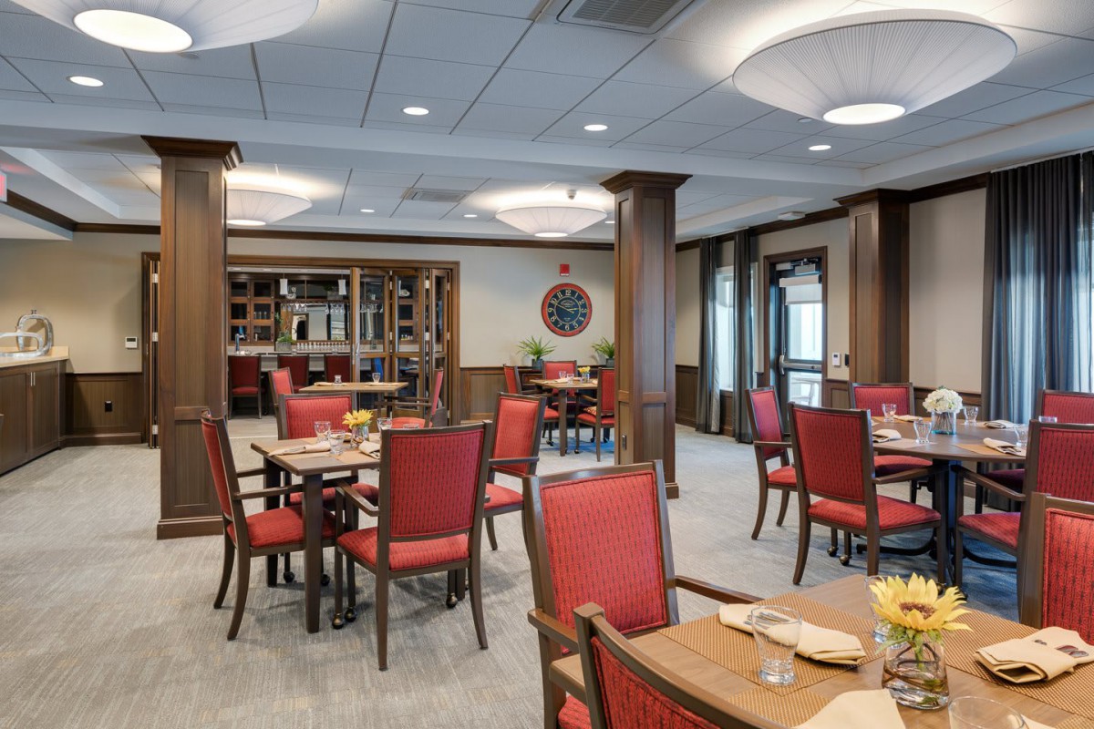 A cozy dining area with red chairs and wooden tables, featuring elegant lighting.