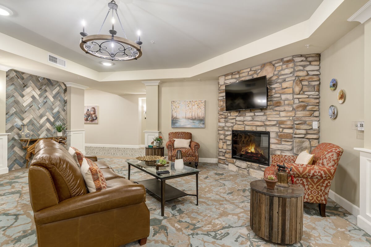 A cozy living room featuring a stone fireplace and modern decor, with comfortable seating and a chandelier overhead.